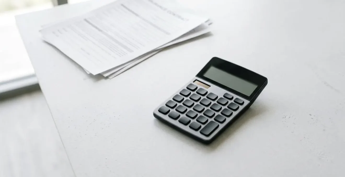 Vue en plongée sur une calculatrice et des documents de contrat d'assurance illustrant le calcul comparatif entre franchise fixe et proportionnelle